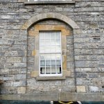 Window with yellowish-grey stone surround and set in a grey stone wall