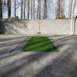 Hexagonal paving leading to curved memorial wall with a gold cross in the center
